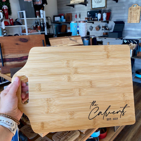 Bamboo handle cutting board with custom engraving held up with gift store shelfs in the background