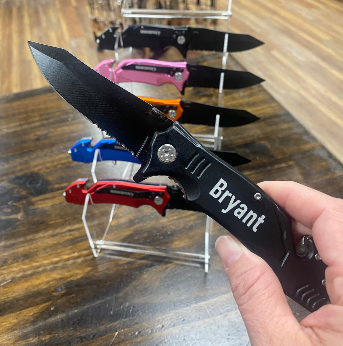 Person holding a black pocket knife with 'Bryant' engraving in a store setting.