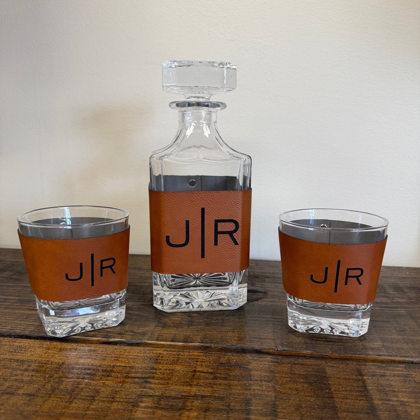 Three clear glass bottles with brown leather wraps labeled 'J/R' on a wooden surface.
