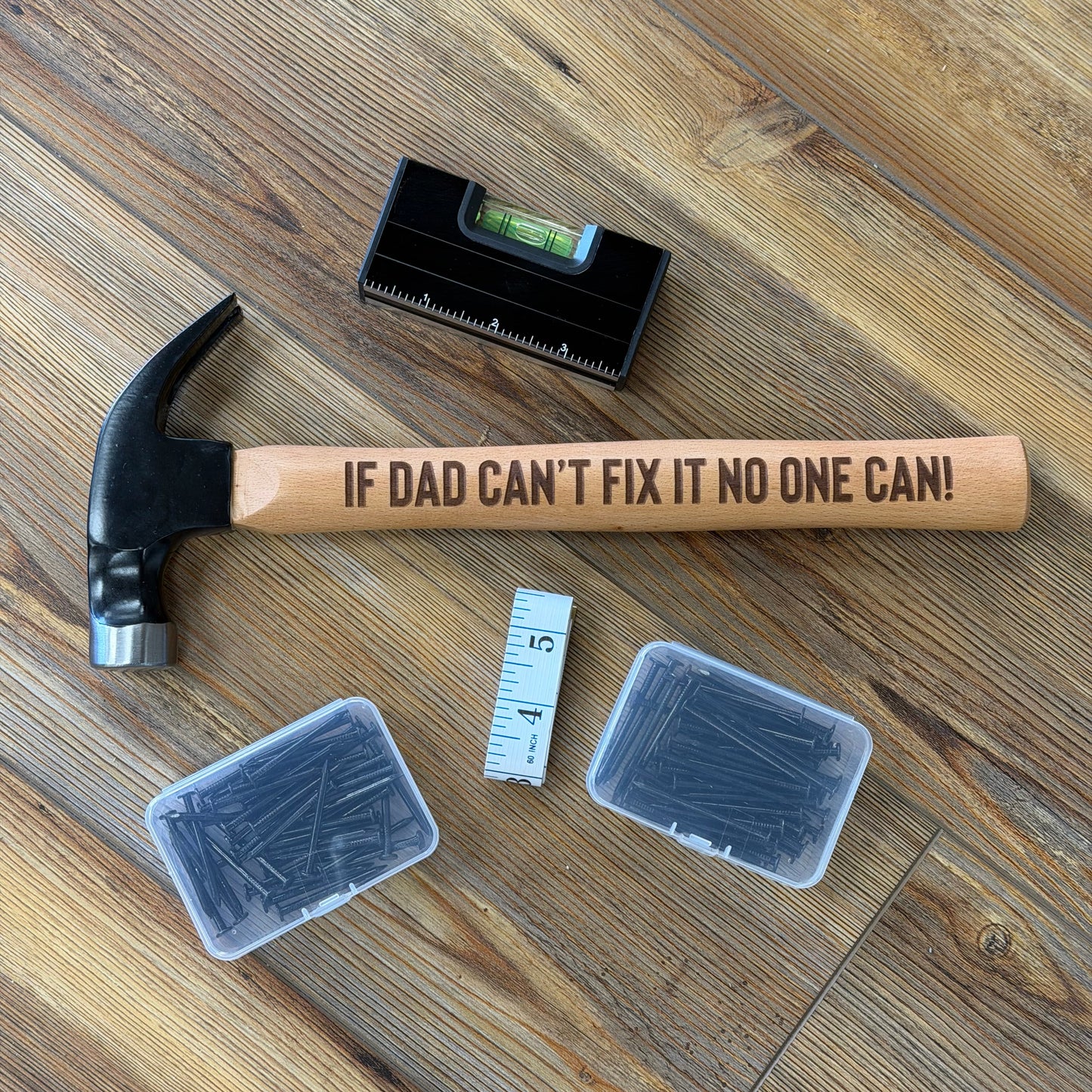 Hammer with a humorous handle on a wooden floor, surrounded by tools and containers.