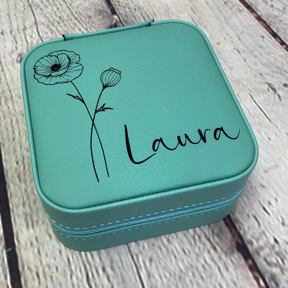 Teal case with floral design and 'Laura' text on a wooden surface