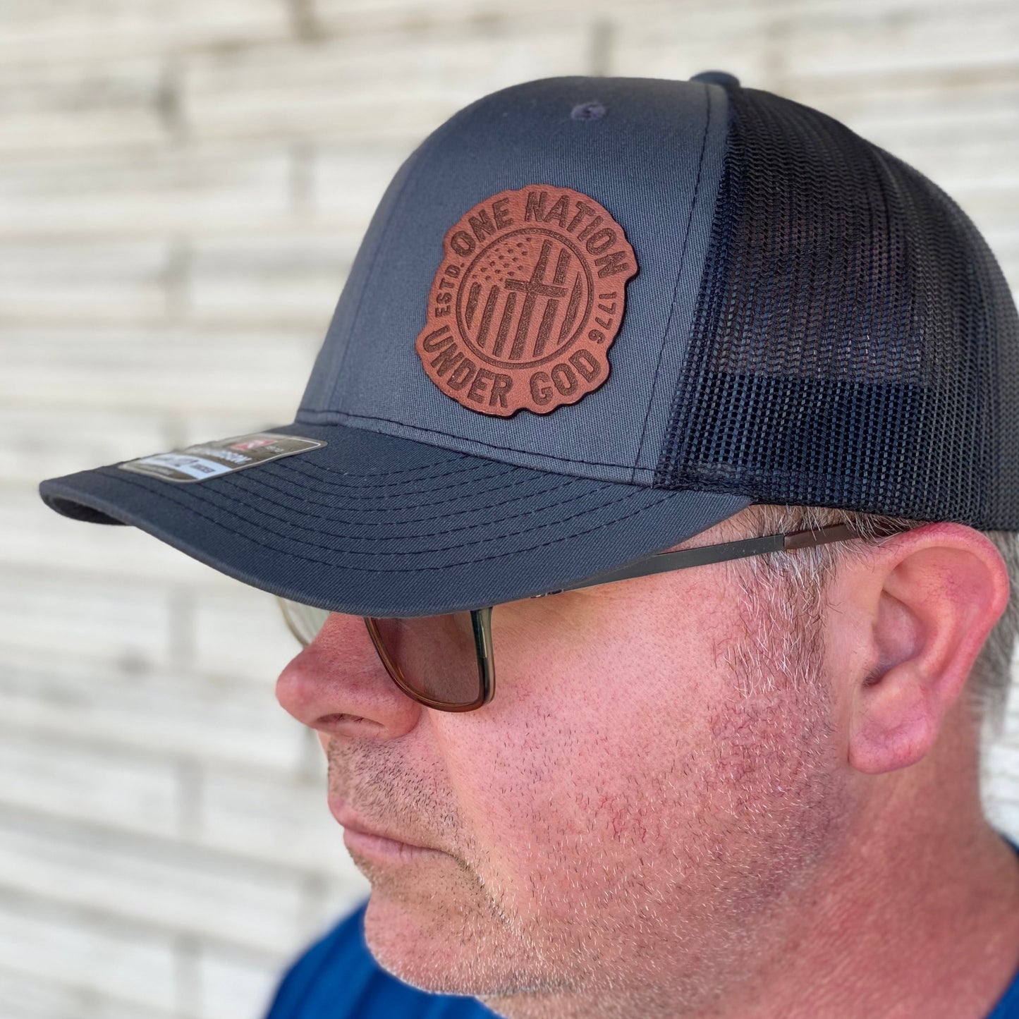 Man wearing A black and gray 'One Nation Under God' Richardson 112 trucker hat with a leather patch on the front.