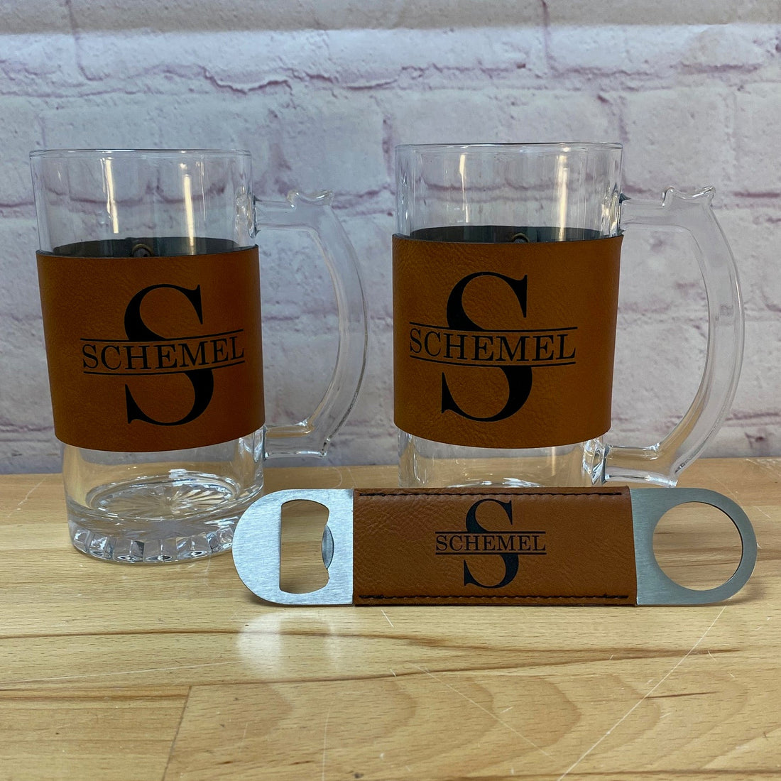 Two clear glass tumblers with brown leather sleeves and a bottle opener on a wooden surface.