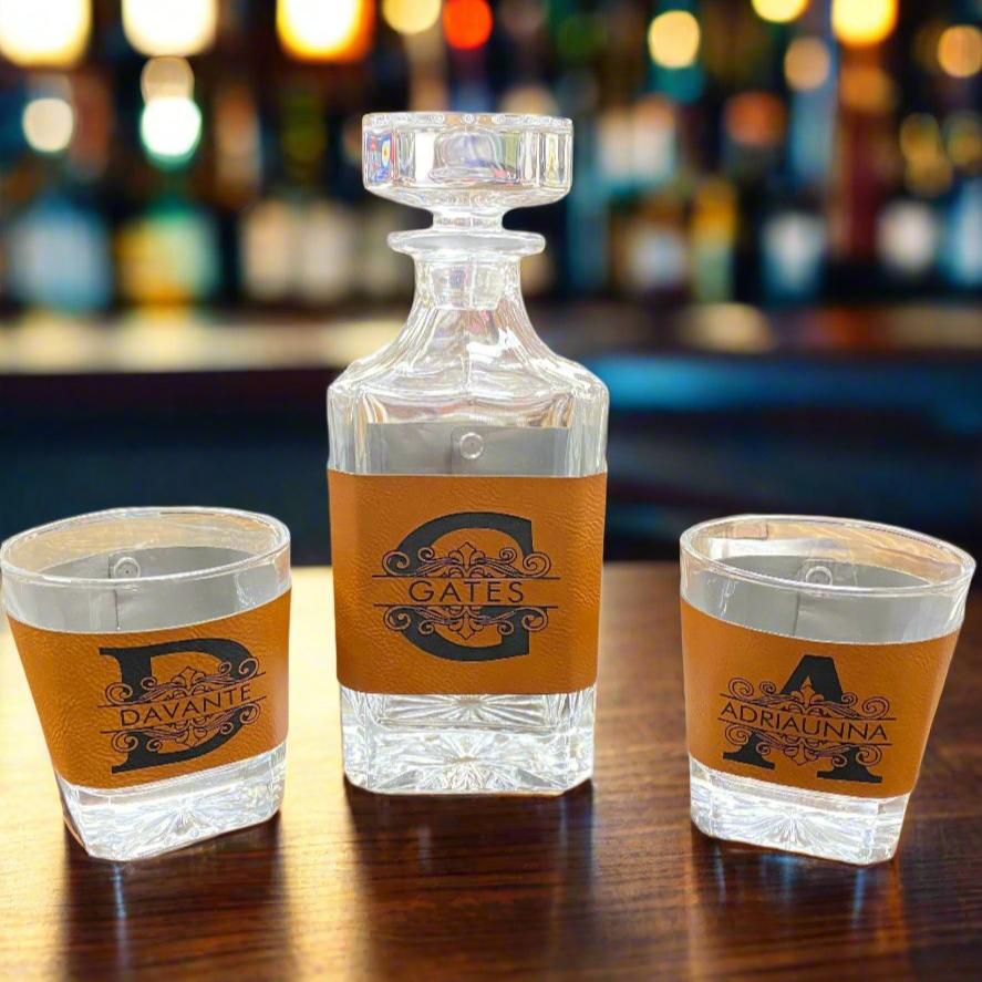 A leather-wrapped decanter set with a glass bottle and two glasses, all engraved with monograms.