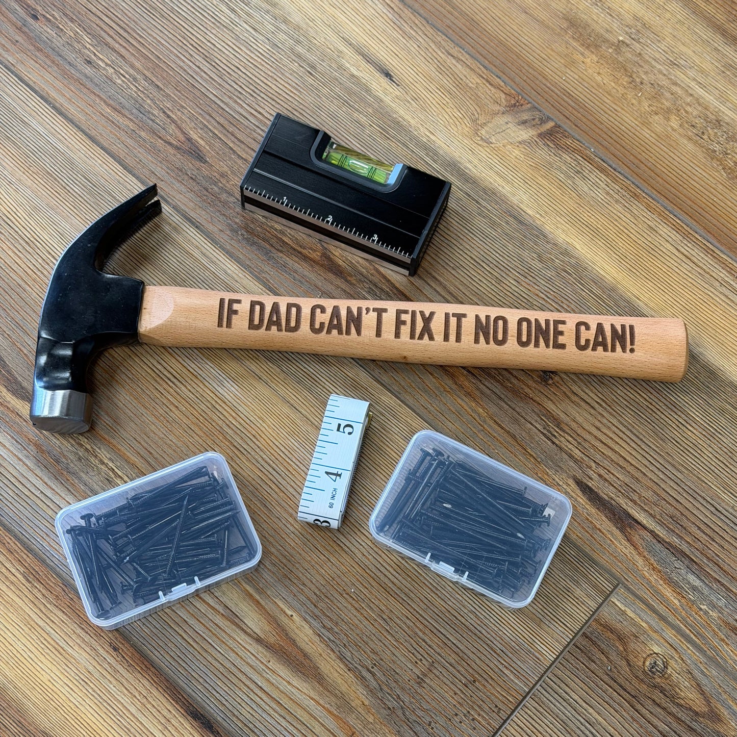Hammer with engraved text on a wooden floor with other tools.