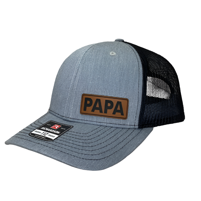 A heather grey and black trucker hat with a leather patch on the front that reads 'Papa'.