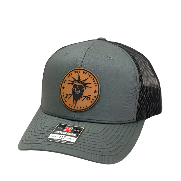 A gray 'Richardson 112' trucker hat with a black leather patch on the front featuring an engraved design.